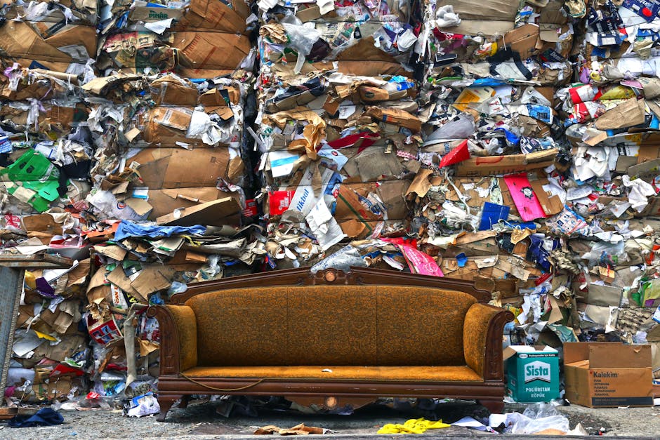 An old, worn-out armchair with a wooden frame and fabric upholstery featuring a plaid pattern, placed outdoors on a sandy, dry terrain. The chair's fabric is torn and frayed, exposing padding and stuf